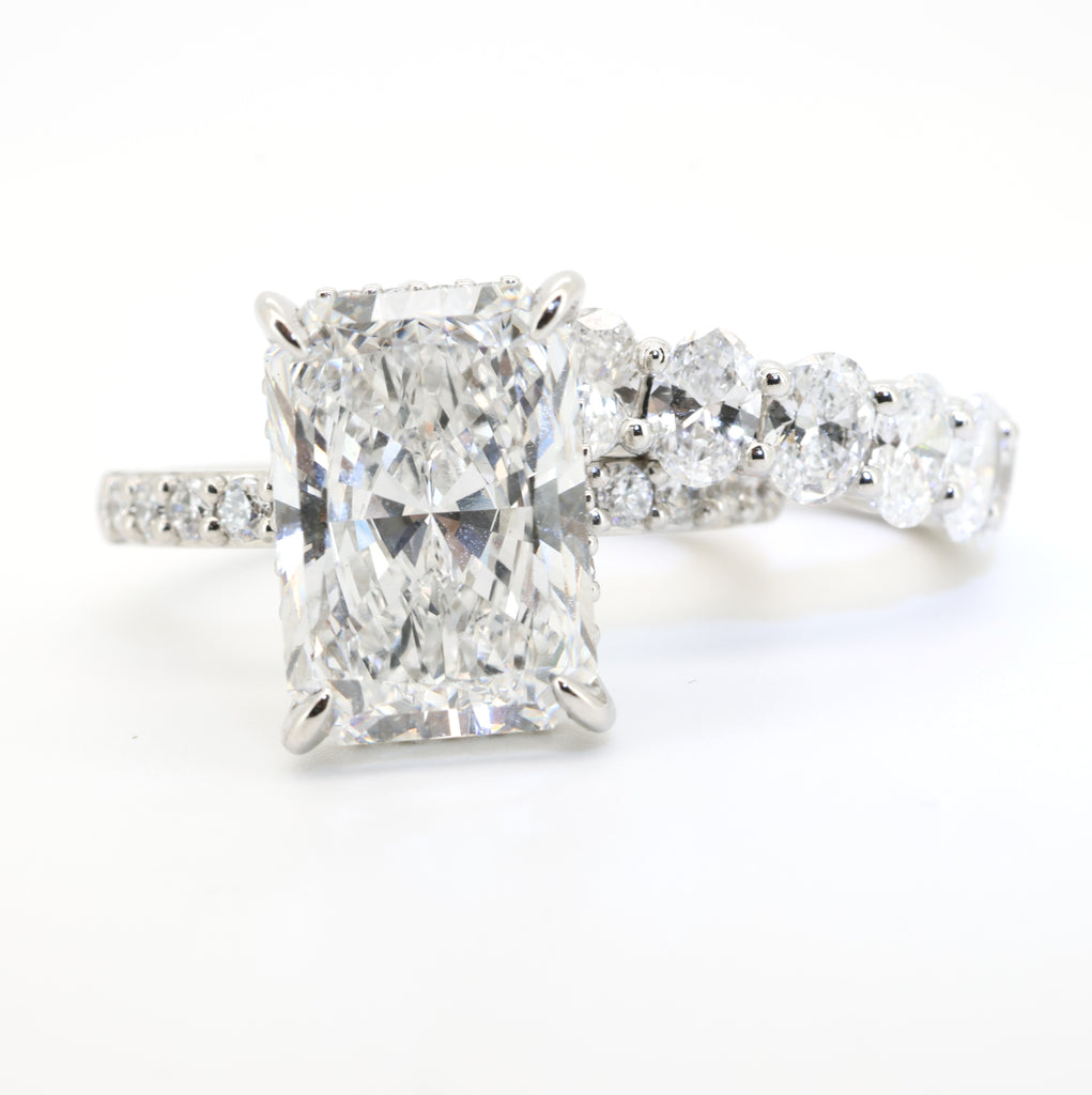 Diamond ring with a clear radiant cut diamond gemstone on a white background with an oval diamond wedding and with 9 oval diamonds